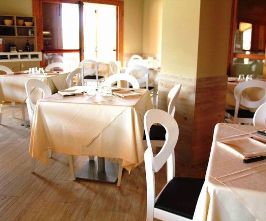 Sala da pranzo con tavoli apparecchiati, sedie bianche e ambiente luminoso.