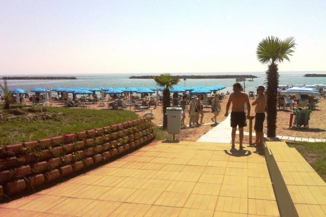 Spiaggia con ombrelloni blu, persone e palme vicino al mare.