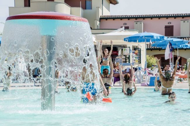 Piscina con getto d'acqua e persone che nuotano e si divertono.