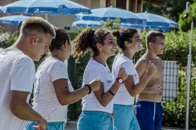 Un gruppo di persone in tenuta sportiva allegre e che camminano all'aperto vicino a ombrelloni blu.