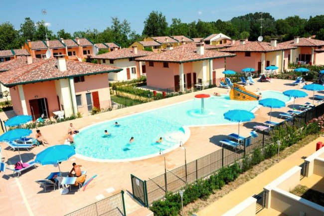 Una piscina circondata da lettini e ombrelloni blu, con villette sullo sfondo.