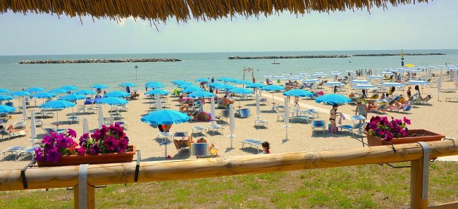 Una spiaggia con ombrelloni blu e sdraio, vista sul mare con barriere di frangimento.