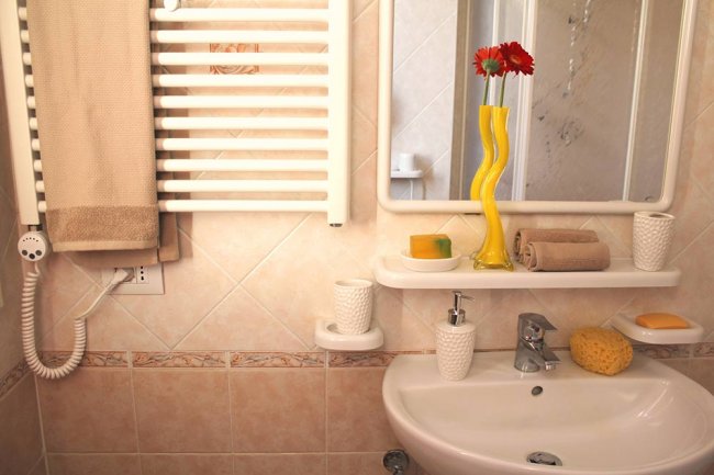 Bagno con specchio, lavandino, termosifone e decorazioni, tra cui fiori rossi in un vaso giallo.