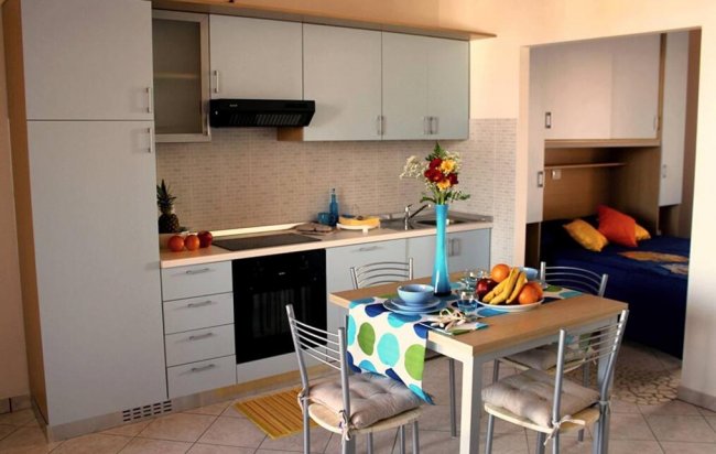 Cucina moderna con tavolo apparecchiato, fiori, frutta e divano blu visibili sullo sfondo.