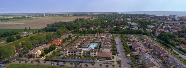 Vista aerea di un complesso residenziale con piscine, circondato da verde e altre abitazioni.