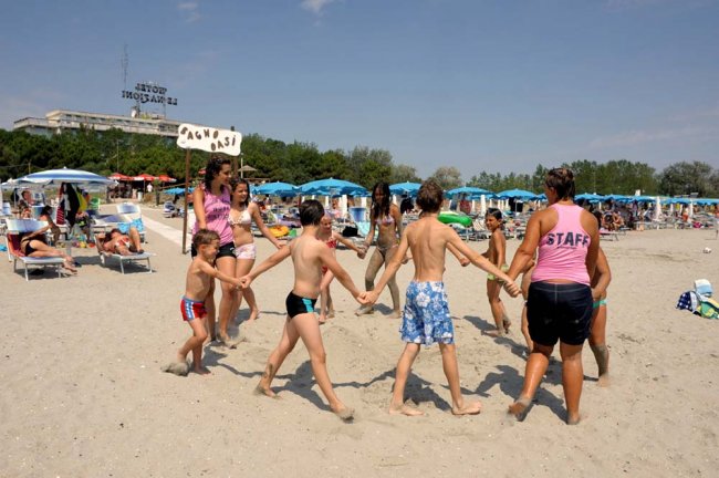 Persone giocano in cerchio su una spiaggia soleggiata.