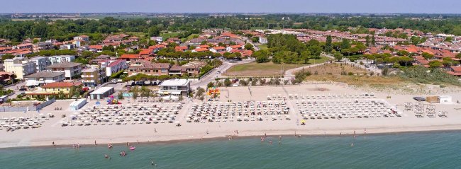 Spiaggia con ombrelloni e villette sullo sfondo.