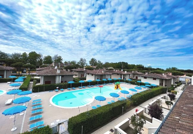 Un complesso residenziale con piscina, molte sdraio blu e cielo nuvoloso.