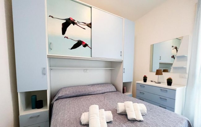 Stanza con letto matrimoniale, armadio con immagini, specchio e cassetti.