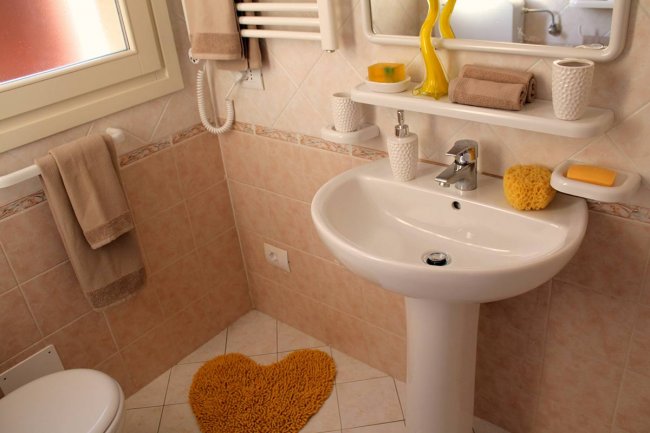 Bagno con lavello, specchio, accessori beige e gialli, e tappetino a forma di cuore.