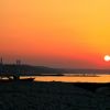 Una spiaggia con torretta di salvataggio e bandiere al tramonto, sole sull'orizzonte.