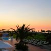 Piscina e area relax con palme al tramonto, vista mare in lontananza.