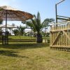 Area all'aperto con ombrelloni di paglia, recinzione di legno e piante tropicali.