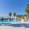 Piscina circondata da palme e sedie a sdraio. Edifici bianchi sullo sfondo.
