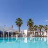 Ampia piscina con palme e pergole. Edifici bianchi circostanti.
