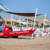 Una spiaggia con una barca di salvataggio rossa e ombrelloni beige.