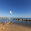 Spiaggia con una bandiera bianca e una barriera frangiflutti.