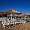 Lettini e ombrelloni di paglia su una spiaggia sabbiosa sotto il cielo blu.