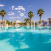 Piscina con acqua cristallina, circondata da palme e ombrelloni bianchi.
