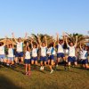 Gruppo di persone che saltano in un prato tra palme, sorridenti e felici.