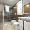 Un bagno moderno con doccia a vetri, lavabo e WC, tonalità marroni e pavimento chiaro.