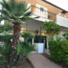 Edificio moderno con piante tropicali intorno e un balcone al piano superiore.