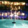 Piscina illuminata di notte con una fontana al centro e persone sullo sfondo.