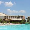 Piscina esterna con ponte di legno e hotel sullo sfondo, cielo azzurro e poche nuvole.