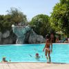 Una piscina con una cascata di roccia e persone che nuotano.