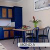 Cucina con mobili blu, tavolo con quattro sedie, e pianta con fiori rossi.