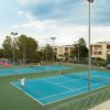 Campi da tennis all'aperto con persone che giocano, circondati da edifici e alberi.