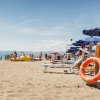 Spiaggia affollata con ombrelloni blu, sedie a sdraio e persone che si godono il sole e il mare.