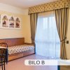 Camera d'hotel con due letti singoli, tavolo e sedie, tende e decorazioni a parete.