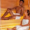 Due persone in una sauna, avvolte in asciugamani, che sorridono e conversano.