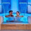 Due persone sorridenti immerse in una piscina illuminata di blu.