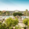 Giardino di un resort con piscine e ombrelloni, circondato da alberi e strutture alberghiere.