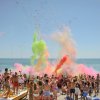 Una folla sulla spiaggia lancia polveri colorate in aria.