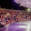 Un pubblico numeroso in un anfiteatro all'aperto, illuminato di notte.