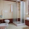 Bagno con doccia angolare in vetro, lavabo e bidet, rifiniture in marrone.