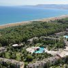 Vista aerea di un resort con piscine, giardini e la spiaggia. Mare e montagne sullo sfondo.