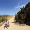 Un sentiero sabbioso vicino al mare con persone che pedalano in bicicletta.