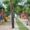 Area giochi con scivoli colorati e tavoli da picnic tra alberi.