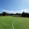 Campo sportivo all'aperto con erba sintetica circondato da reti e alberi.