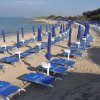 Spiaggia sabbiosa con file ordinate di lettini blu e ombrelloni chiusi.