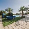 Una barca blu posizionata su un prato fra palme, con una piscina visibile sullo sfondo.