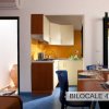Cucina e sala da pranzo con tavolo apparecchiato e mobili moderni. Porta aperta sul patio.