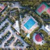 Vista aerea di un villaggio turistico con piscina centrale e campi da tennis.