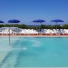 Piscina con ombrelloni blu e lettini bianchi.