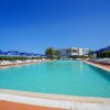 Piscina circondata da lettini, ombrelloni blu e cespugli verdi.