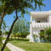 Edificio bianco con balcone e giardino verde con alberi.